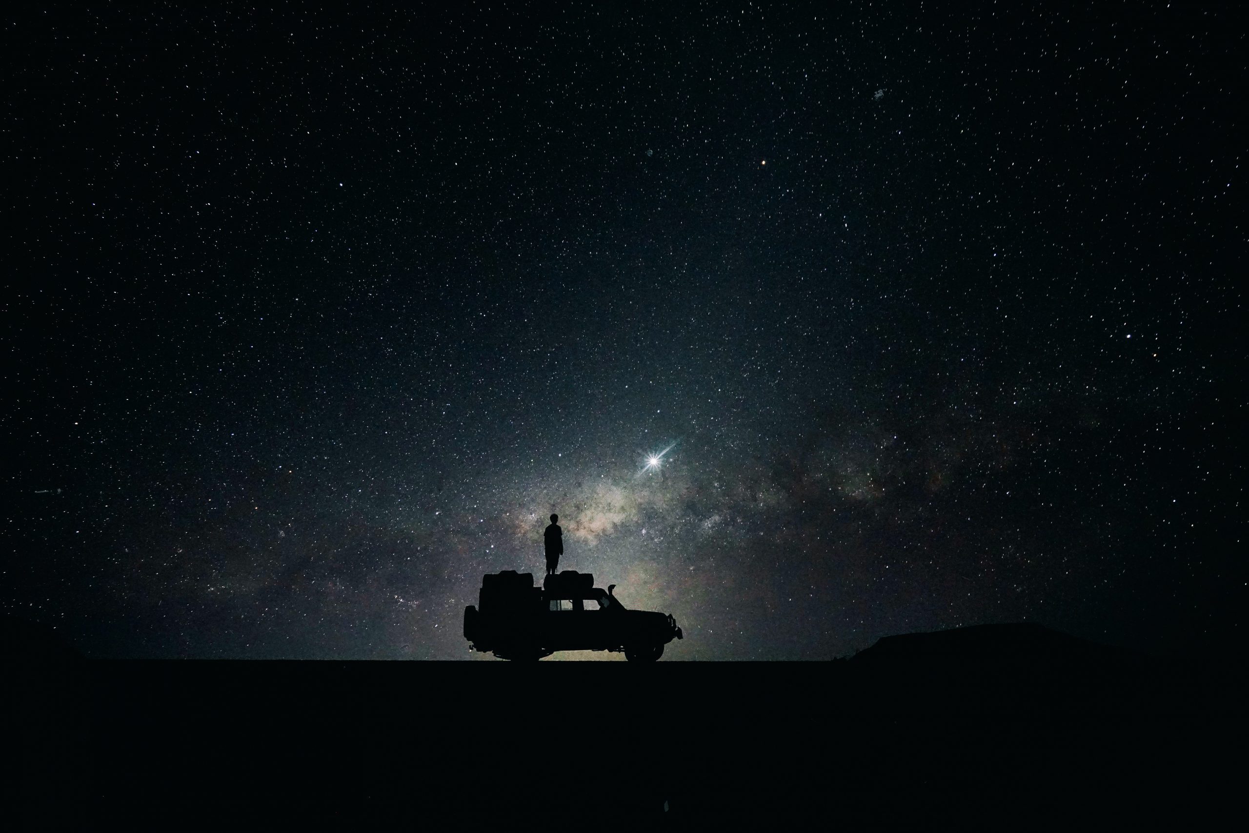 Silhouette of man standing on car in front of night sky